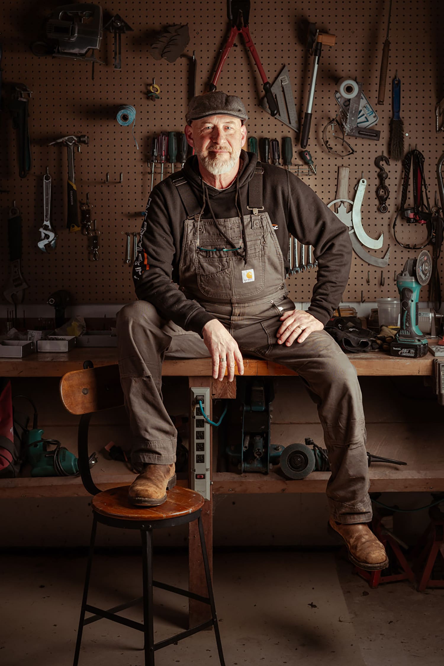 Tom sitting on a stool looking into camera, wearing work clothes.