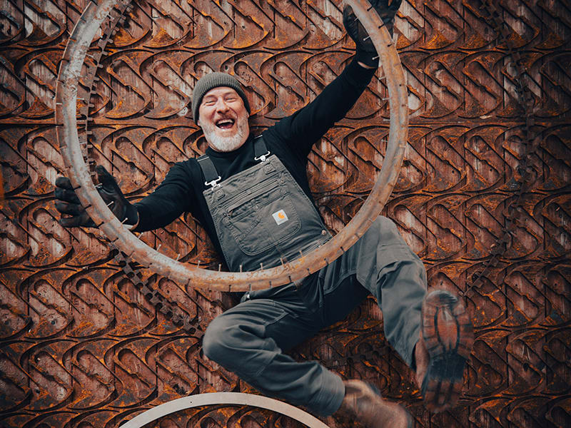 Portrait of artist lying on metal shapes, laughing and holding up a large metal circle.
